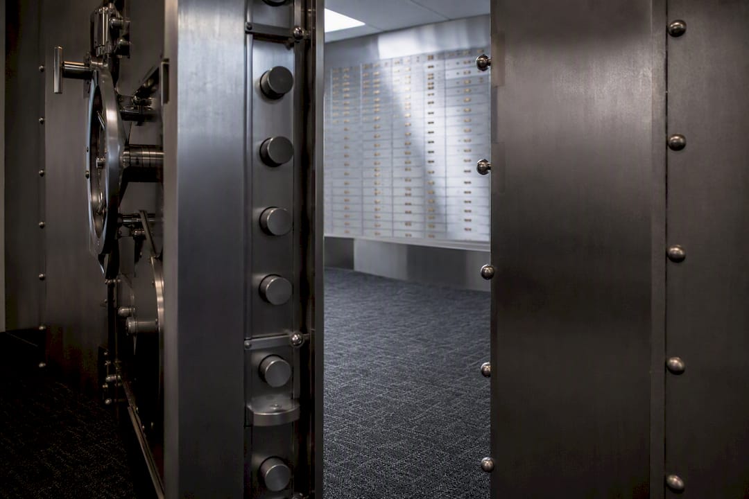 Partially open bank vault door with safety deposit boxes